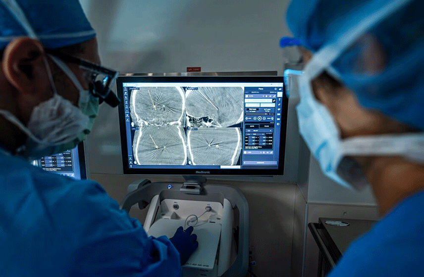 Two clinicians use a deep brain stimulation system while viewing brain imaging scans on a monitor.