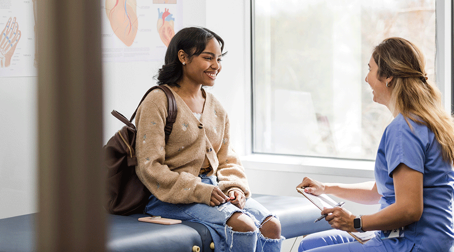 Caregiver talks with a young patient during an appointment in a clinical exam room.